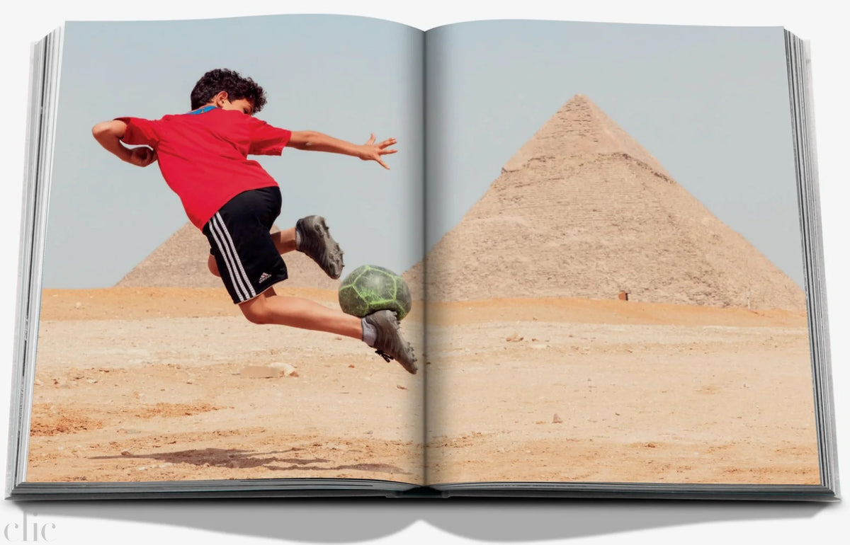 Open book showing a photo of a child playing with a ball in front of pyramids