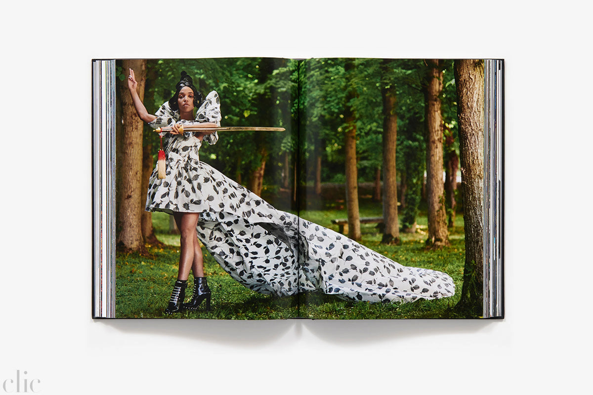 FKA Twigs in a long, flowing, patterned dress, standing in a forest.